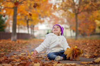 Adorable little girl in the park, playing with leaves
