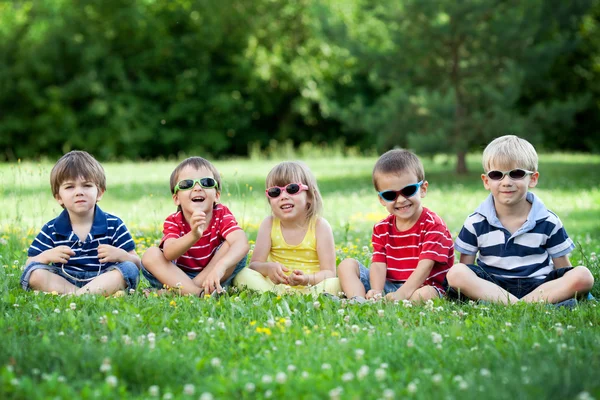 Cinque adorabili bambini, sdraiati sull'erba, sorridenti, che si divertono — Foto Stock