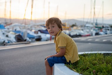 Sweet little child, toddler boy, sitting and watching the harbor