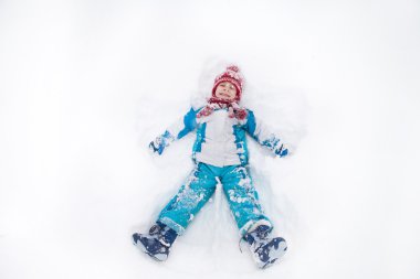 Adorable little boy in blue jacket, red hat and scarf,  lying on clipart