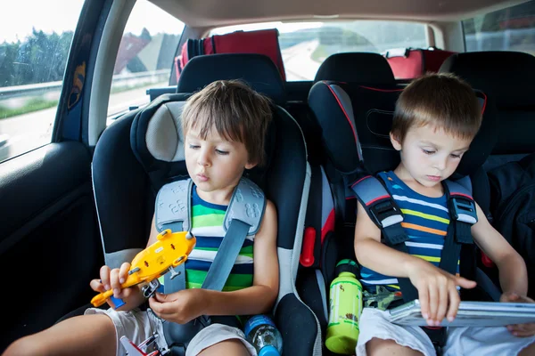 Dos niños en asientos de coche, viajando en coche y jugando con juguetes y —  Fotos de Stock