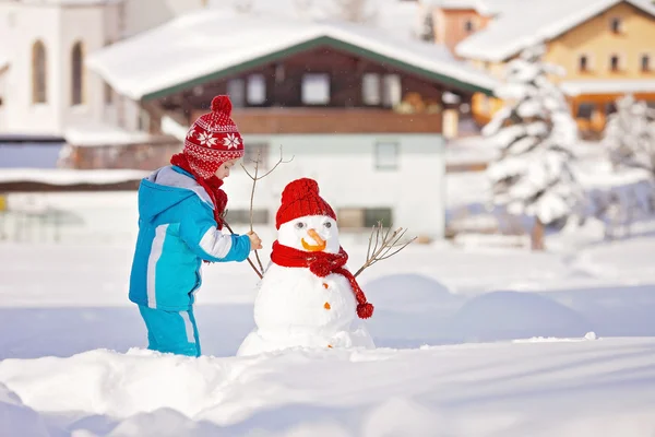 Felice bel bambino che costruisce pupazzo di neve in giardino, inverno — Foto Stock