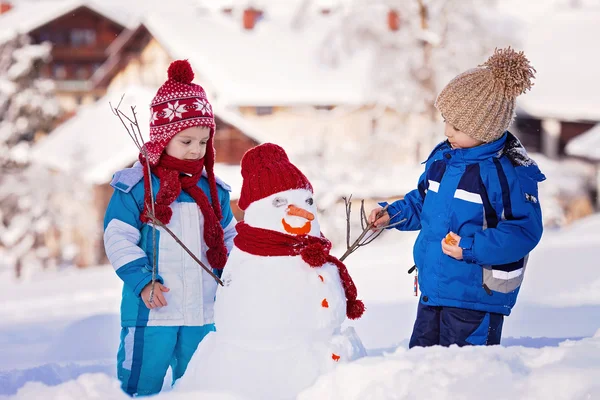 Crianças bonitas felizes, irmãos, construindo boneco de neve no jardim , — Fotografia de Stock