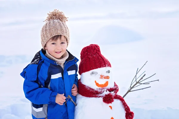 Criança bonita feliz construindo boneco de neve no jardim, inverno — Fotografia de Stock