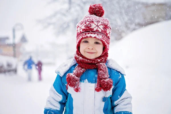 Ładny mały chłopiec w niebieskim zimowy kombinezon, grając odkryty w śniegu — Zdjęcie stockowe