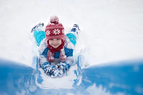 Mignon petit garçon, descendre un toboggan enneigé — Photo