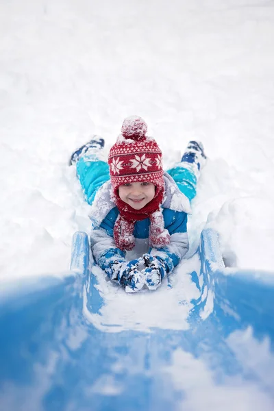 Schattige kleine jongen, naar beneden een besneeuwde dia — Stockfoto