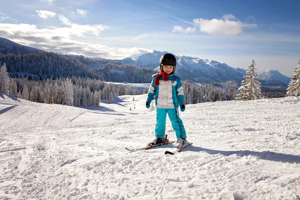 Очаровательный мальчик в синей куртке и шлеме, катается на лыжах — стоковое фото