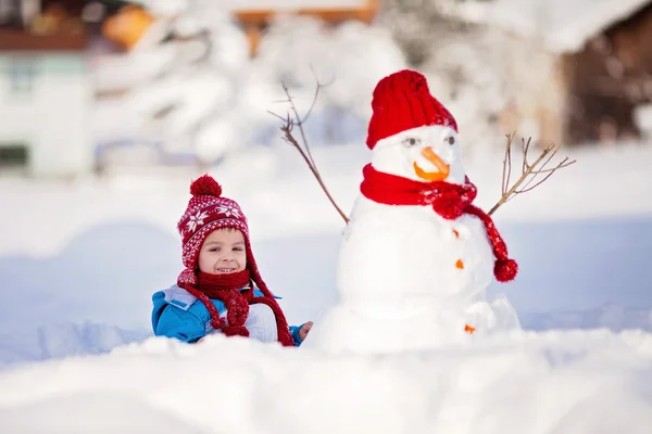 Happy beautiful child building snowman in garden, winter — Stock Photo, Image