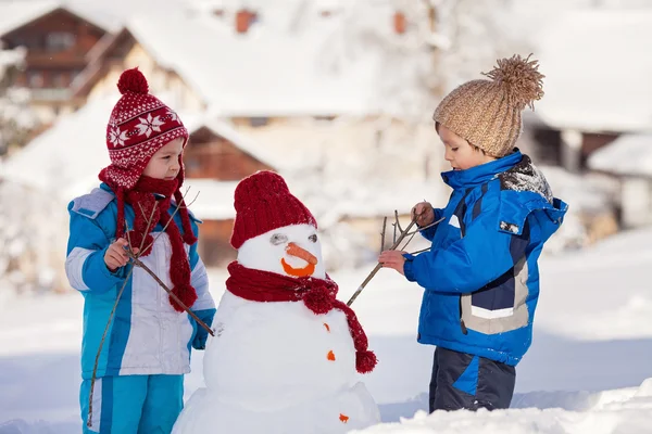 Feliz hermoso niños, hermanos, construcción de muñeco de nieve en el jardín , — Foto de Stock