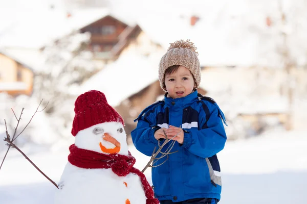 Joyeux bel enfant construction bonhomme de neige dans le jardin, hiver — Photo