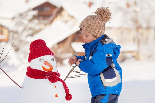 Felice bel bambino che costruisce pupazzo di neve in giardino, inverno — Foto Stock