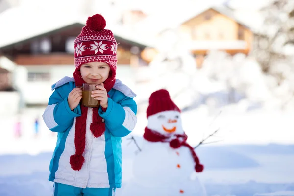 Happy beautiful child building snowman in garden, winter time, h