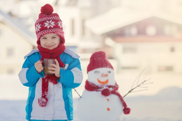 Happy beautiful child building snowman in garden, winter time, h