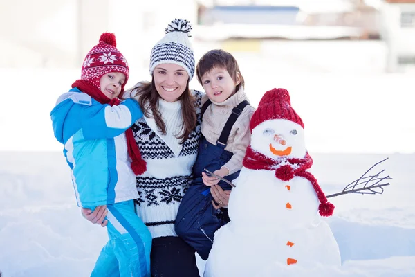 Happy beautiful family building snowman in garden, winter time,
