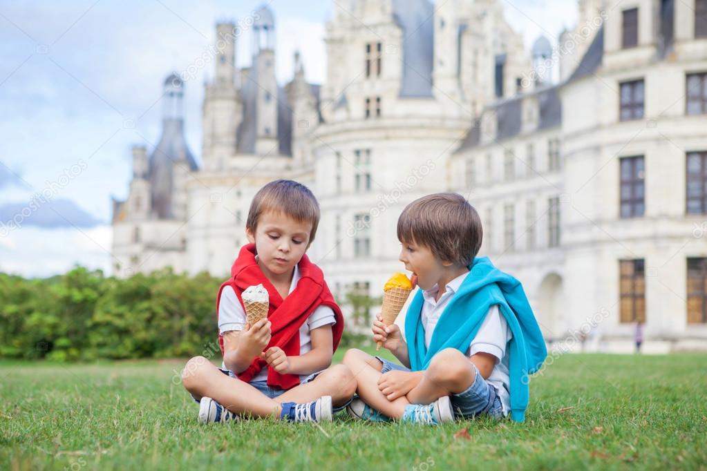 Two adorable boys in casual clothing, eating ice cream sitting o