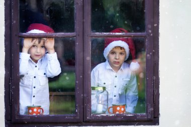Noel Baba'yı bekleyen bir pencereden bakarak iki yakışıklı çocuk,