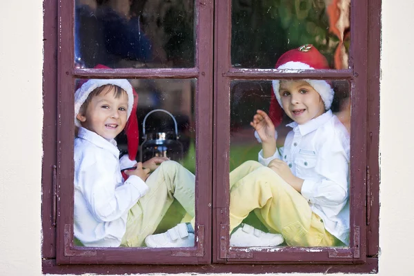 Zwei süße Jungen, die durch ein Fenster schauen und auf den Weihnachtsmann warten — Stockfoto
