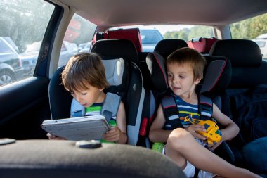 Two boy in children car seats, traveling by car and playing with