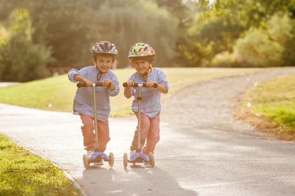 İki sevimli çocuklar, rekabet scooter, parkta açık sürme, — Stok fotoğraf