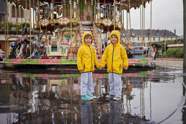 Two sweet children, boy brothers, watching carousel in the rain, — Zdjęcie stockowe