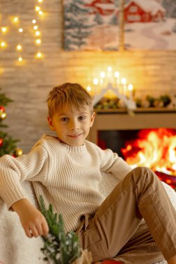 Sevimli anaokulu çocuğu, şöminenin önünde oturuyor, Noel hediyesini tutuyor ve evde kitap, eğlence ve mutluluk okuyor.