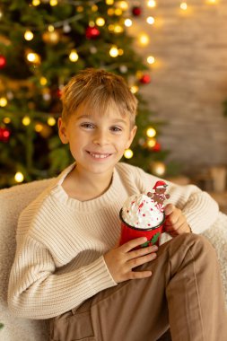 Sevimli anaokulu çocuğu, şöminenin önünde oturuyor, Noel hediyesini tutuyor ve evde kitap, eğlence ve mutluluk okuyor.
