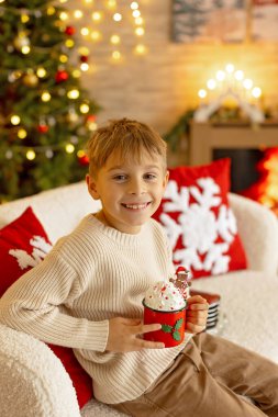 Sevimli anaokulu çocuğu, şöminenin önünde oturuyor, Noel hediyesini tutuyor ve evde kitap, eğlence ve mutluluk okuyor.