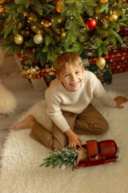 Sevimli anaokulu çocuğu, şöminenin önünde oturuyor, Noel hediyesini tutuyor ve evde kitap, eğlence ve mutluluk okuyor.