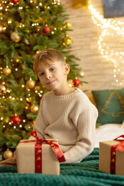 Sevimli anaokulu çocuğu, şöminenin önünde oturuyor, Noel hediyesini tutuyor ve evde kitap, eğlence ve mutluluk okuyor.