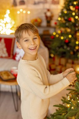 Sevimli anaokulu çocuğu, şöminenin önünde oturuyor, Noel hediyesini tutuyor ve evde kitap, eğlence ve mutluluk okuyor.