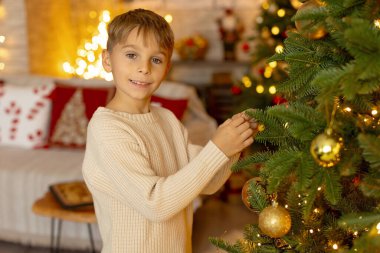 Sevimli anaokulu çocuğu, şöminenin önünde oturuyor, Noel hediyesini tutuyor ve evde kitap, eğlence ve mutluluk okuyor.