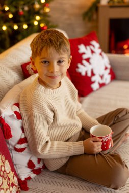 Sevimli anaokulu çocuğu, şöminenin önünde oturuyor, Noel hediyesini tutuyor ve evde kitap, eğlence ve mutluluk okuyor.