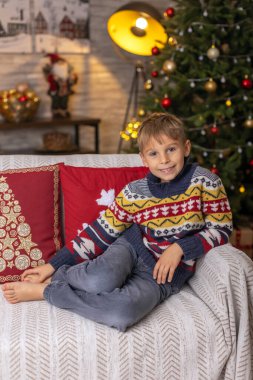 Sevimli anaokulu çocuğu, şöminenin önünde oturuyor, Noel hediyesini tutuyor ve evde kitap, eğlence ve mutluluk okuyor.