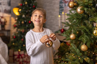 Sevimli anaokulu çocuğu, şöminenin önünde oturuyor, Noel hediyesini tutuyor ve evde kitap, eğlence ve mutluluk okuyor.