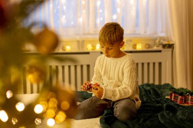 Sevimli anaokulu çocuğu, şöminenin önünde oturuyor, Noel hediyesini tutuyor ve evde kitap, eğlence ve mutluluk okuyor.
