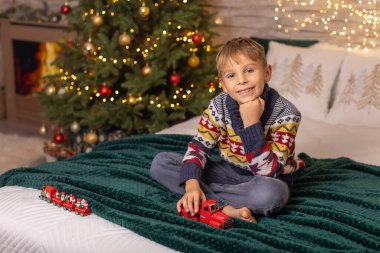 Sevimli anaokulu çocuğu, şöminenin önünde oturuyor, Noel hediyesini tutuyor ve evde kitap, eğlence ve mutluluk okuyor.