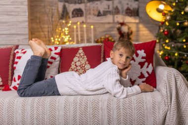 Sevimli anaokulu çocuğu, şöminenin önünde oturuyor, Noel hediyesini tutuyor ve evde kitap, eğlence ve mutluluk okuyor.