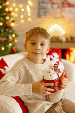 Sevimli anaokulu çocuğu, şöminenin önünde oturuyor, Noel hediyesini tutuyor ve evde kitap, eğlence ve mutluluk okuyor.