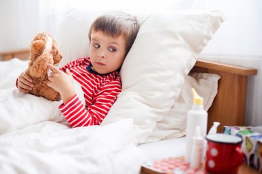 Sick child boy lying in bed with a fever, resting clipart