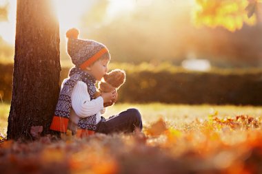 Adorable little boy with teddy bear in park on autumn day clipart