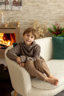 Hoş bir okul çocuğu, süslü bir odada oturuyor, kış dekorasyonu, şömine ve çiçekler, huzur ve sessizliğin tadını çıkarıyor.