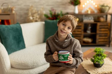 Hoş bir okul çocuğu, süslü bir odada oturuyor, kış dekorasyonu, şömine ve çiçekler, huzur ve sessizliğin tadını çıkarıyor.