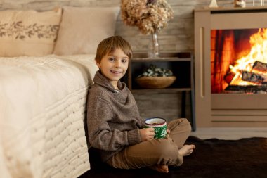 Hoş bir okul çocuğu, süslü bir odada oturuyor, kış dekorasyonu, şömine ve çiçekler, huzur ve sessizliğin tadını çıkarıyor.
