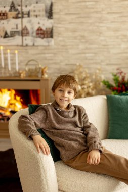 Hoş bir okul çocuğu, süslü bir odada oturuyor, kış dekorasyonu, şömine ve çiçekler, huzur ve sessizliğin tadını çıkarıyor.