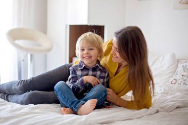 Anne, küçük çocuk ve yavru köpek, yatağa uzanıp birlikte kitap okuyorlar, mutlu aile zamanları.