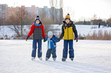 Mutlu çocuklar, parktaki donmuş gölde paten kayıyorlar, kış zamanı.