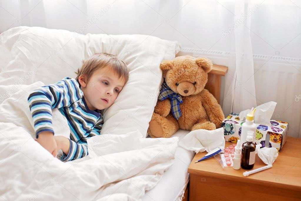 Sick child boy lying in bed with a fever, resting