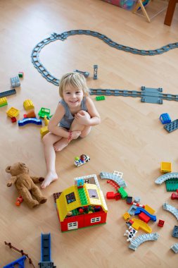 Sevimli çocuk, renkli oyuncak bloklarıyla oynuyor. Güneşli, ferah yatak odasında yerde oturan küçük çocuk oyuncaklardan ev inşa ediyor. Bebekler için eğitici bir oyun