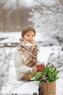 Çocuğum, karlı ormanda kış partisi veriyoruz. Genç bir çocuk, çay içiyor ve çam ağacının dallarıyla ilgileniyordu. Soğuk havada sıcak içecek, kar, soğuk ve açık havada ışık.